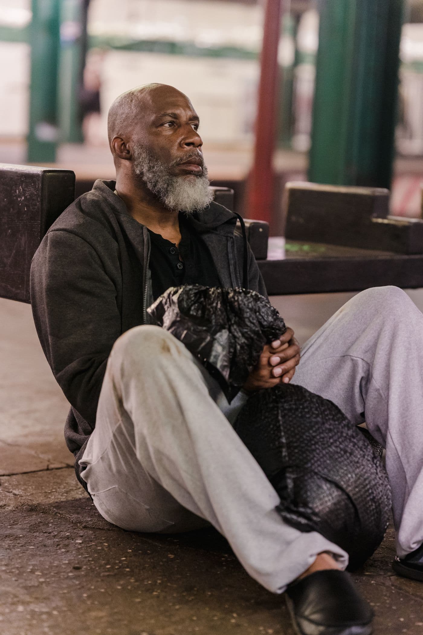 A man sitting outdoors with his belongings gathered beside him.