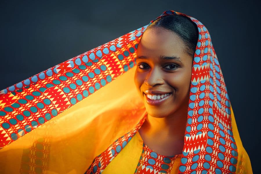 Portrait of a smiling woman in a brightly patterned headscarf.